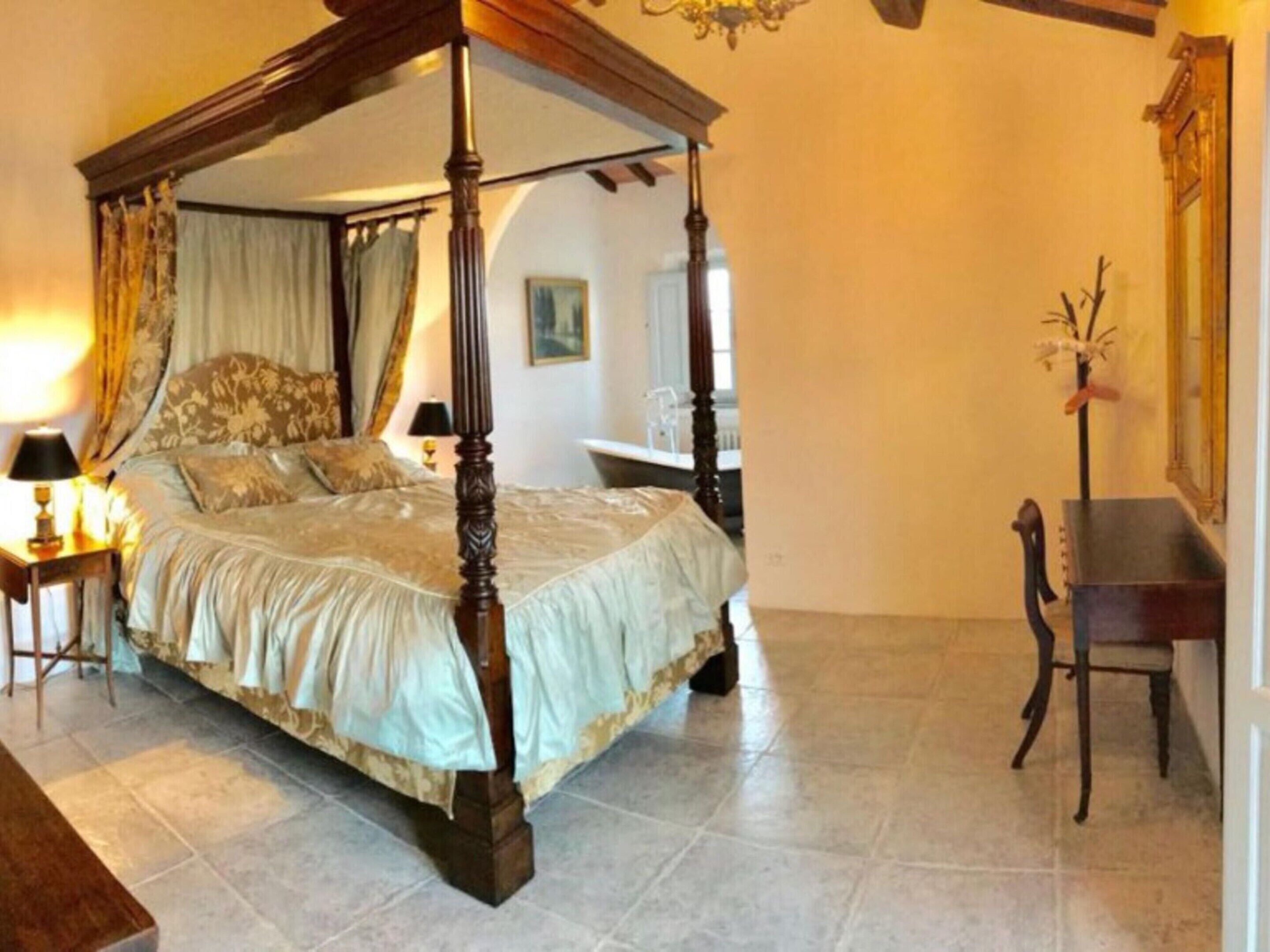 A four-poster bed with a canopy, a nightstand with a lamp, a chair, and a desk with a mirror.