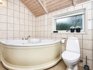 A bathroom with a freestanding bathtub, a toilet, and a window with a view of trees. - 4 Star Holiday Home in Ebeltoft (Ebeltoft)