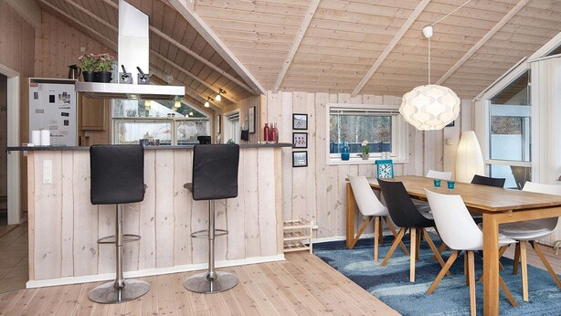 Een moderne keuken met houten kastjes, een bar met krukken, een eettafel met stoelen en een groot raam dat voor natuurlijk licht zorgt.