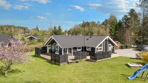 Eenlaags huis met een donker dak en witte raamkozijnen, omringd door een omheinde tuin met een glijbaan en een kleine tuin.