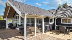 Een overdekt terras buiten met een houten terras, een barbecue en tuinmeubilair.