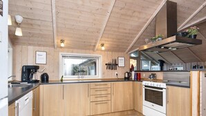 Een moderne keuken met houten kastjes, een inbouwoven en een raam met uitzicht op een huis.
