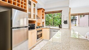 Una cocina moderna con electrodomésticos de acero inoxidable, armarios de madera y un amplio ventanal con vistas al verdor.