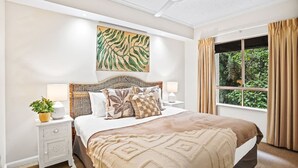 Un dormitorio con una cama grande, un ventilador de techo, una ventana con cortinas y una obra de arte colgada en la pared.