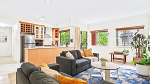 Una sala de estar moderna con un sofá gris, una mesa de centro y una zona de cocina con refrigerador, microondas y armarios.