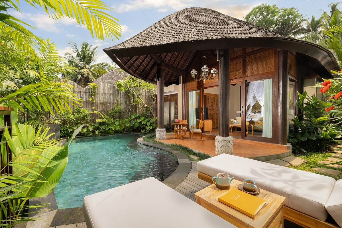 A poolside area with a covered seating area, a lounge chair, and a table with a book and teapot.