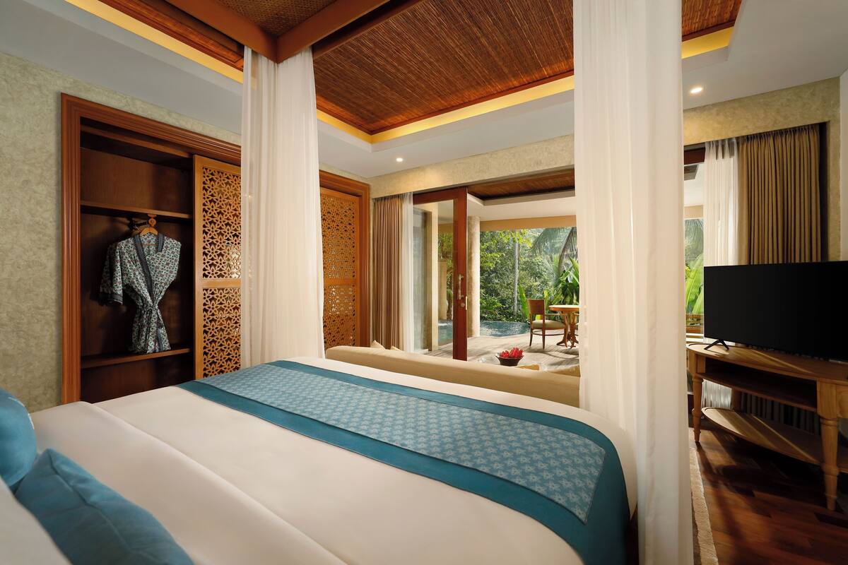 A hotel room with a large bed, a TV, a wardrobe, and a view of the outdoors.