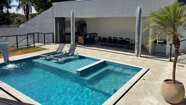 A rectangular swimming pool with two lounge chairs and a potted palm tree. - Desfrute de Momentos Inesquecíveis em Caldas Novas! Casa Aconchegante 3 Suites (Portal das Águas Quentes Caldas Novas)