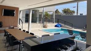 A modern kitchen with a gas stove, a dining table with chairs, and a large window overlooking a swimming pool area. - Desfrute de Momentos Inesquecíveis em Caldas Novas! Casa Aconchegante 3 Suites (Portal das Águas Quentes Caldas Novas)