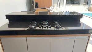 A kitchen with a black countertop, three gas burners, and a wooden backsplash. - Desfrute de Momentos Inesquecíveis em Caldas Novas! Casa Aconchegante 3 Suites (Portal das Águas Quentes Caldas Novas)