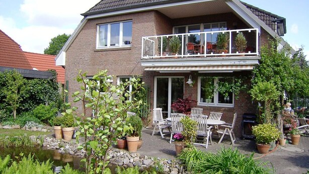 A two-story house with a balcony, a pond, and outdoor furniture.
