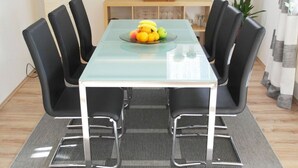 A dining area with a glass table, black chairs, and a fruit bowl.