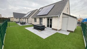 Un edificio moderno con paneles solares, un área de estar cubierta al aire libre y un césped bien cuidado.
