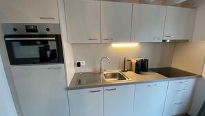 Una cocina moderna con armarios blancos, un lavamanos de acero inoxidable, horno empotrado y placa de inducción negra.
