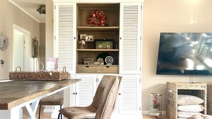 Un comedor con una mesa y sillas de madera, un televisor y una cesta de mimbre con cojines.