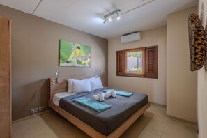 A neatly made bed with white linens and a green blanket, a wall-mounted air conditioner, and a window with wooden shutters. - Spanish Water Apartments - Garden View (Jan Thiel)
