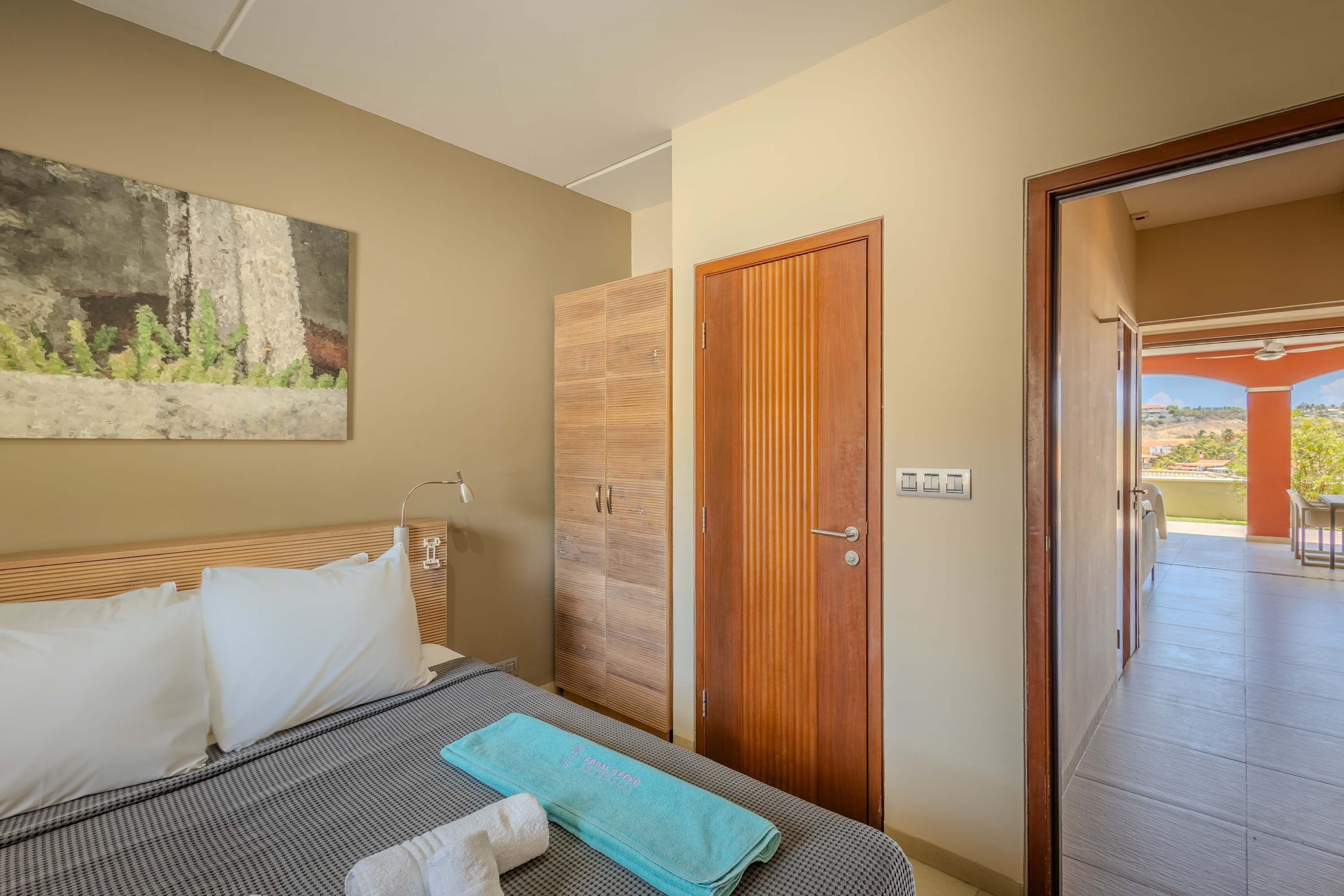Une chambre d’hôtel avec un lit, une armoire en bois, un tableau au mur et une vue sur l’espace extérieur.
