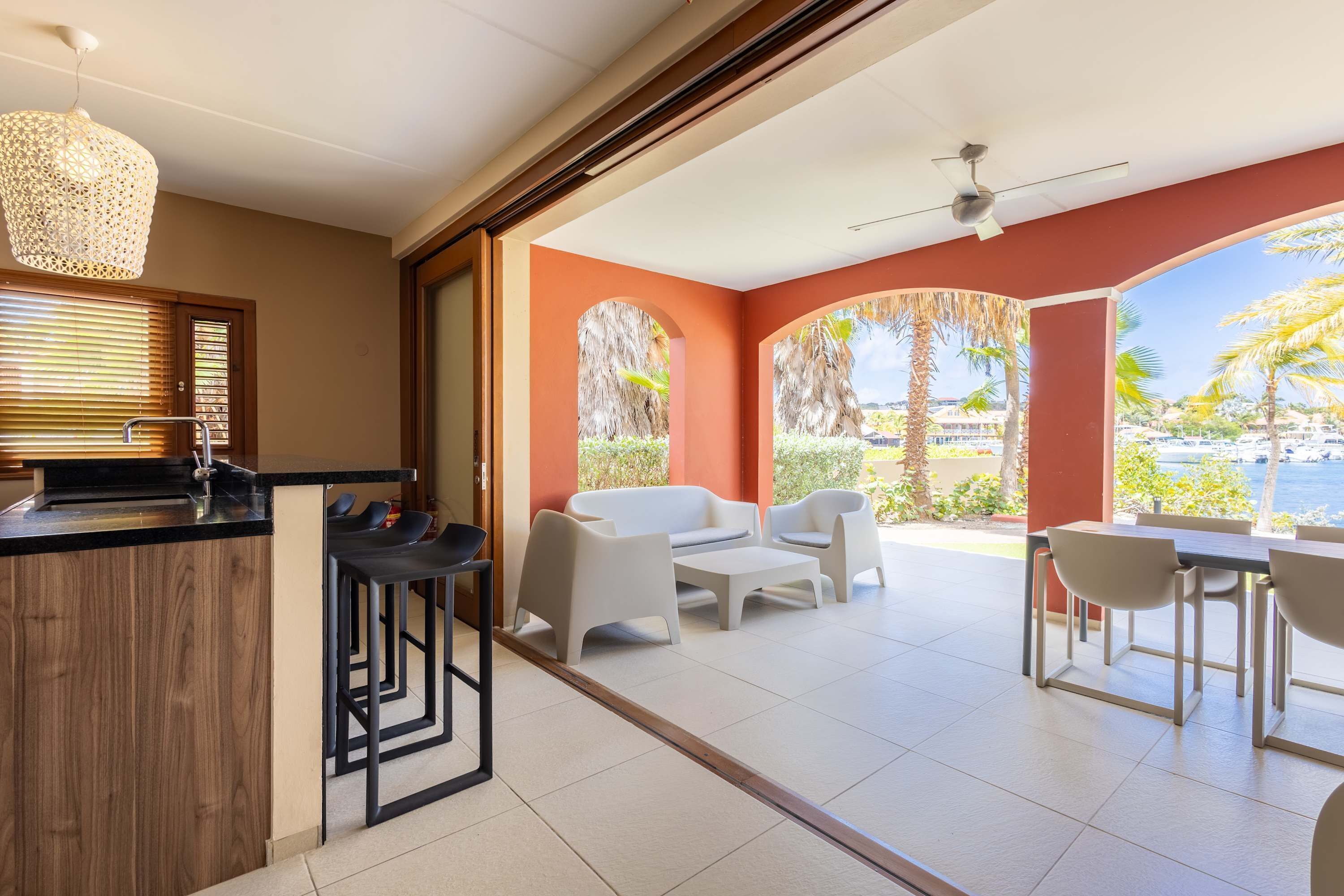 A modern kitchen with a bar area, white furniture, and a view of the sea.