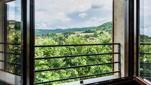 Ein Balkon mit Metallgeländer, der auf eine üppige, grüne Landschaft mit Hügeln und Gebäuden in der Ferne blickt.