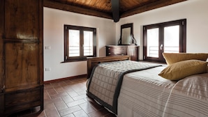 Ein Schlafzimmer mit Holzboden, einem Bett mit gestecktem Überwurf, zwei Fenstern und einer Kommode.