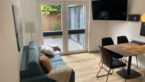 Un salon moderne comprenant un canapé, une table à manger avec des chaises, un téléviseur à écran plat fixé au mur et une porte-fenêtre coulissante donnant sur un espace extérieur.