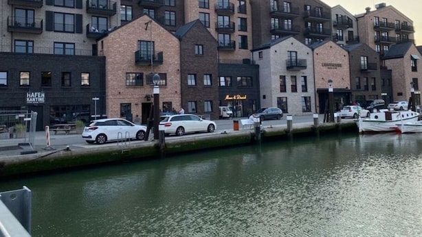 Un bâtiment situé au bord de l’eau, avec plusieurs étages, des balcons et une enseigne indiquant « Hafen Kantine ».