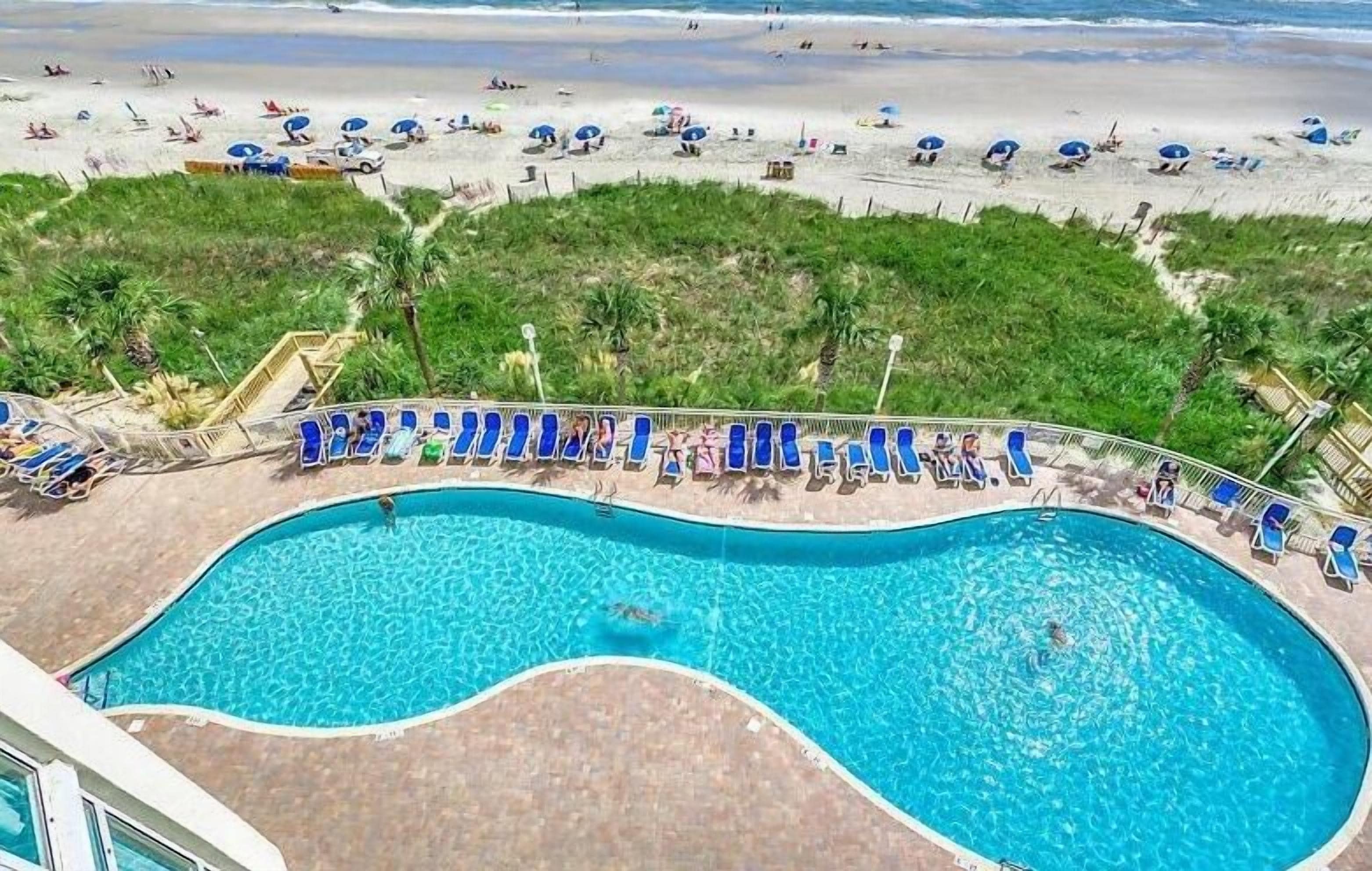 A swimming pool with lounge chairs and a view of the beach.