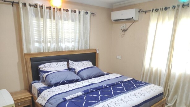 Une chambre à coucher avec un lit, des rideaux, un appareil de climatisation et une table de chevet.
