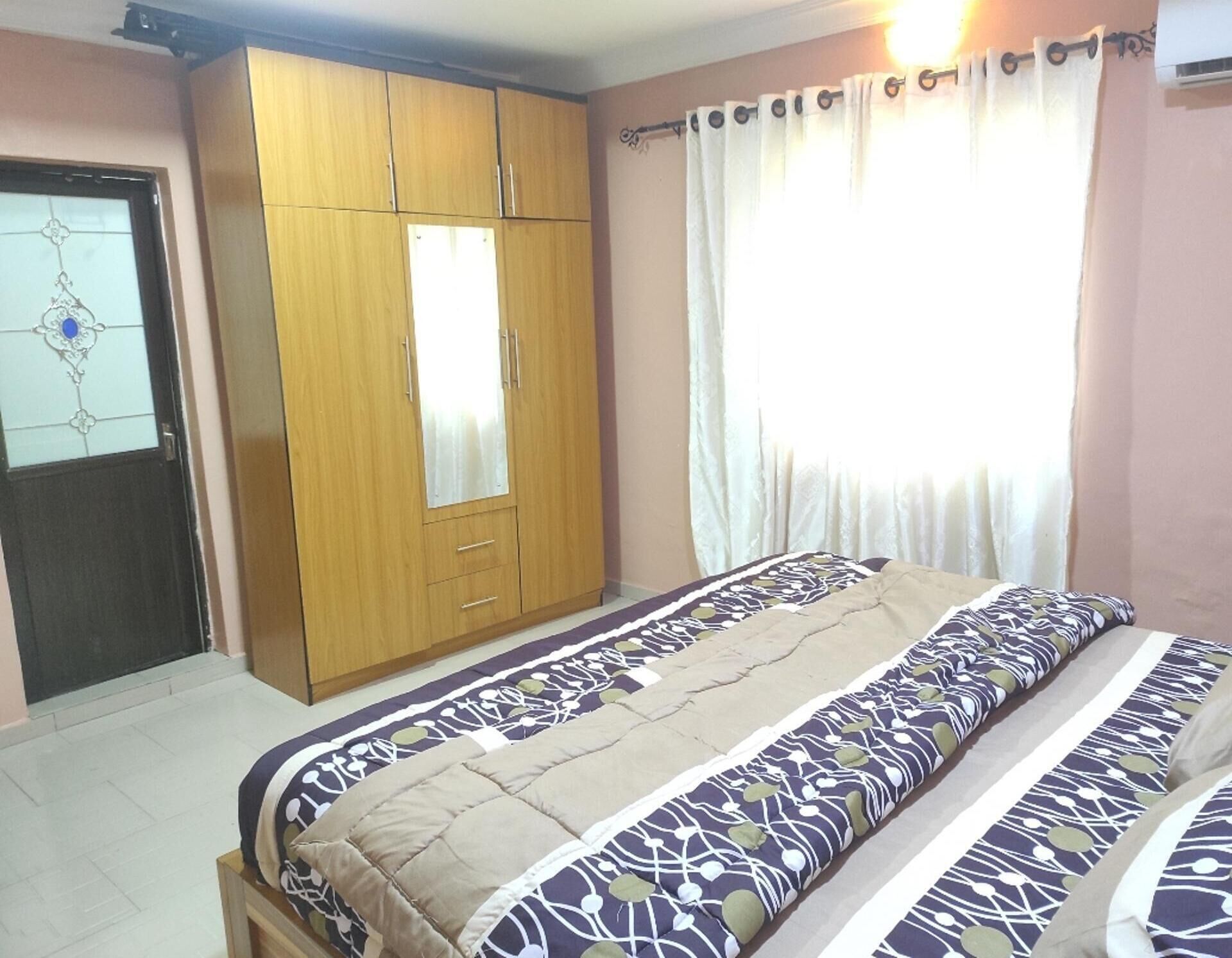 A bedroom with a bed, a wardrobe, a window with curtains, and a door with a glass panel.