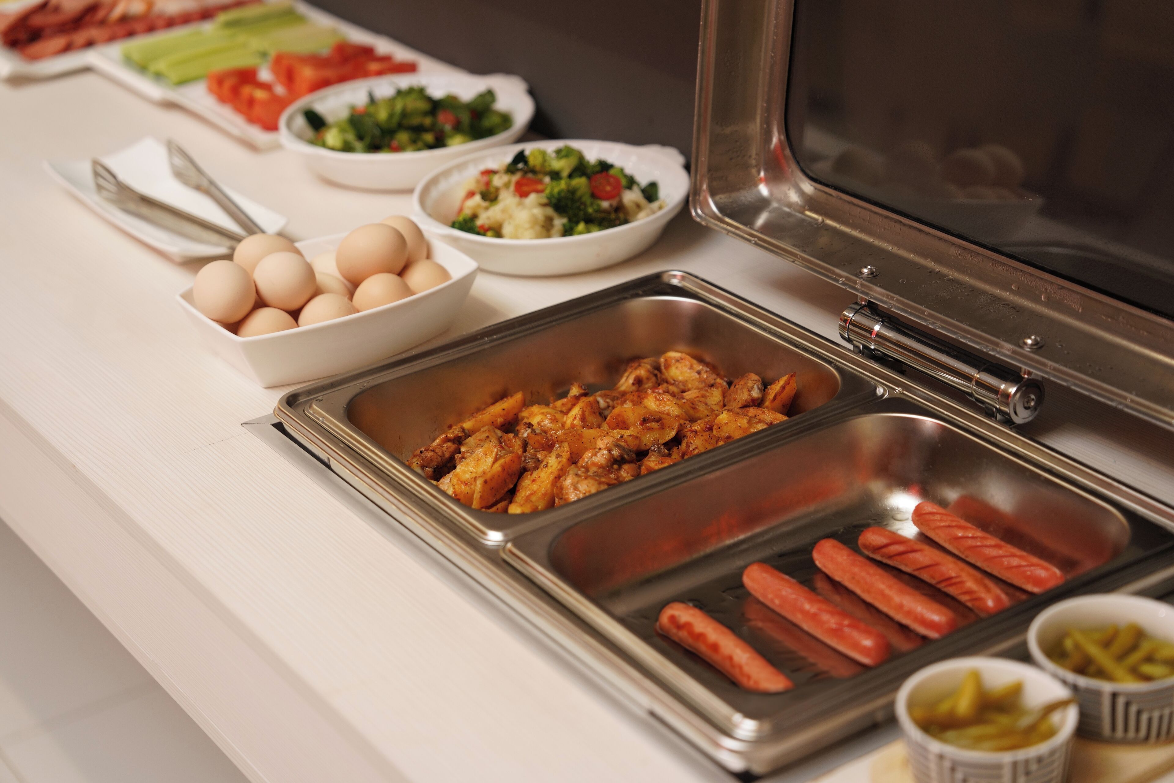 En buffet med flere retter, blandt andet æg, kylling, hotdogs og salater.