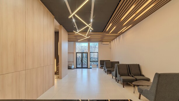 A modern interior with a long reception area, wooden panel walls, and a seating area with grey upholstered chairs.