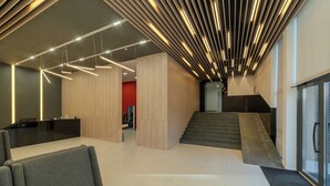 A modern lobby with a reception desk, seating area, and a staircase leading to upper floors.
