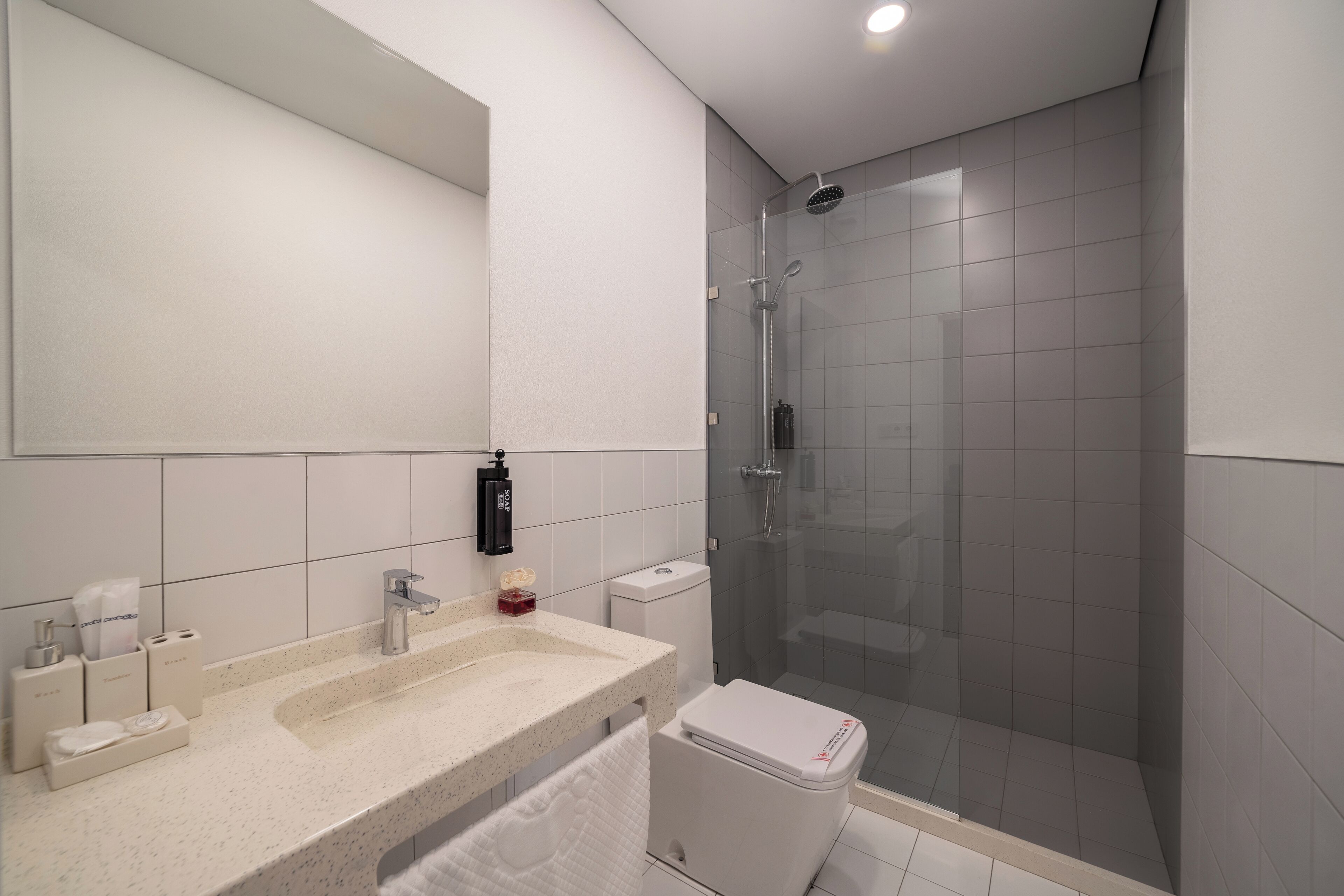 A modern bathroom with a glass-enclosed shower, a large mirror, and a countertop with toiletries.