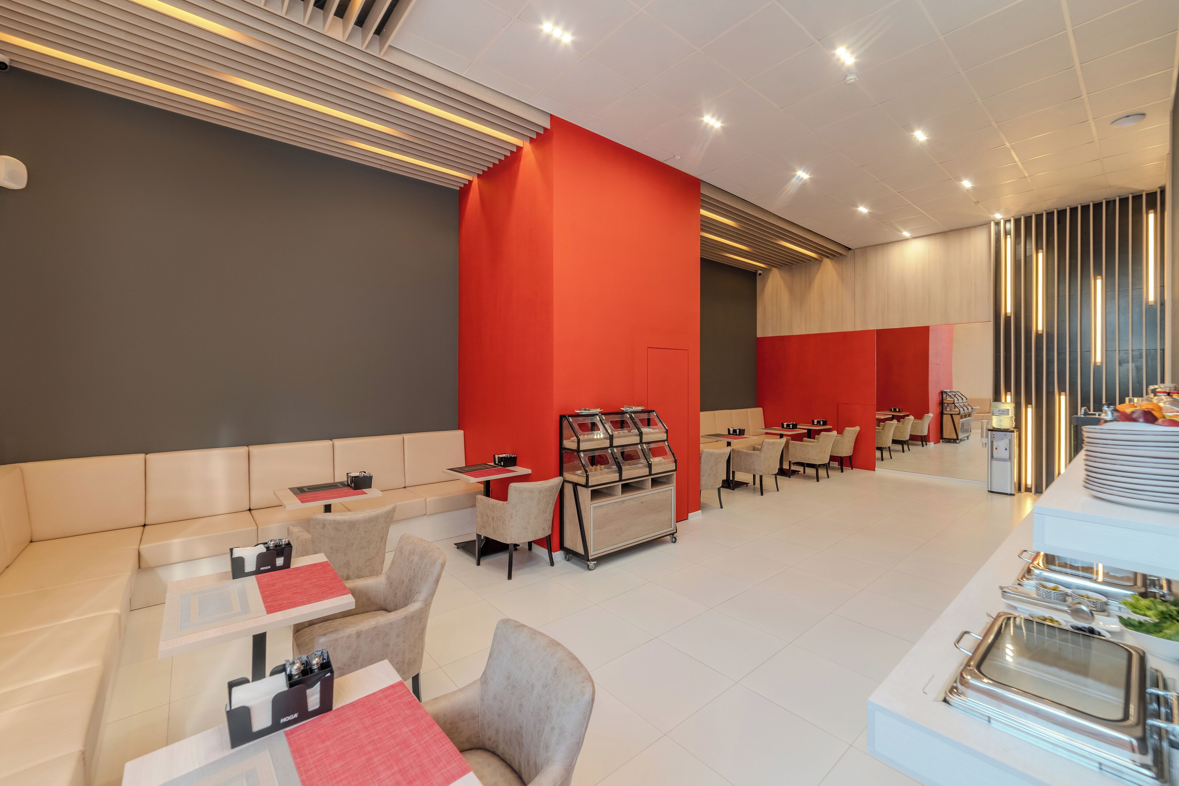 Eine moderne Hotelhalle mit roter Akzentwand, Sitzbereichen und Buffet.