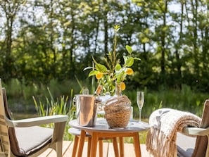 An outdoor table with a metal pitcher, a glass bottle, and a glass of water, surrounded by chairs and a woven basket. - Nice Holiday Home in Kortgene With Garden (Kortgene)