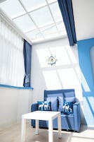 Una habitación moderna con un sofá azul, una mesa blanca y un amplio ventanal con cortinas.