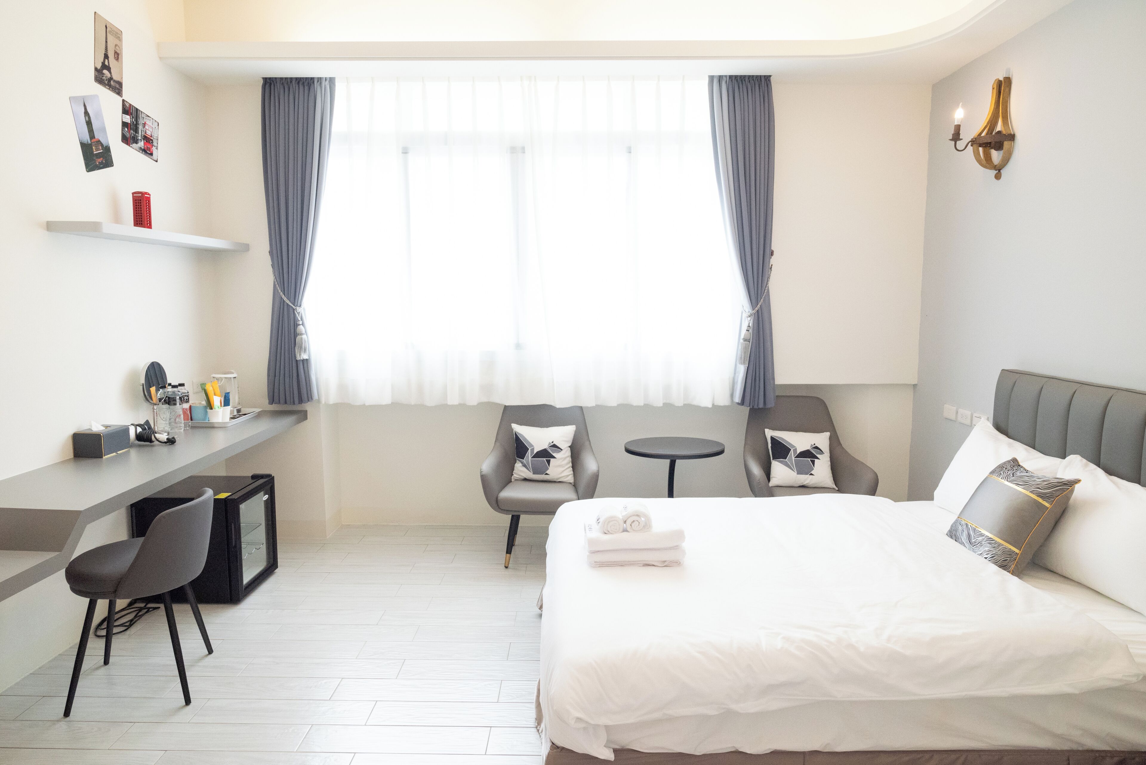 A hotel room with a bed, a desk, two chairs, a small table, and a window with curtains.