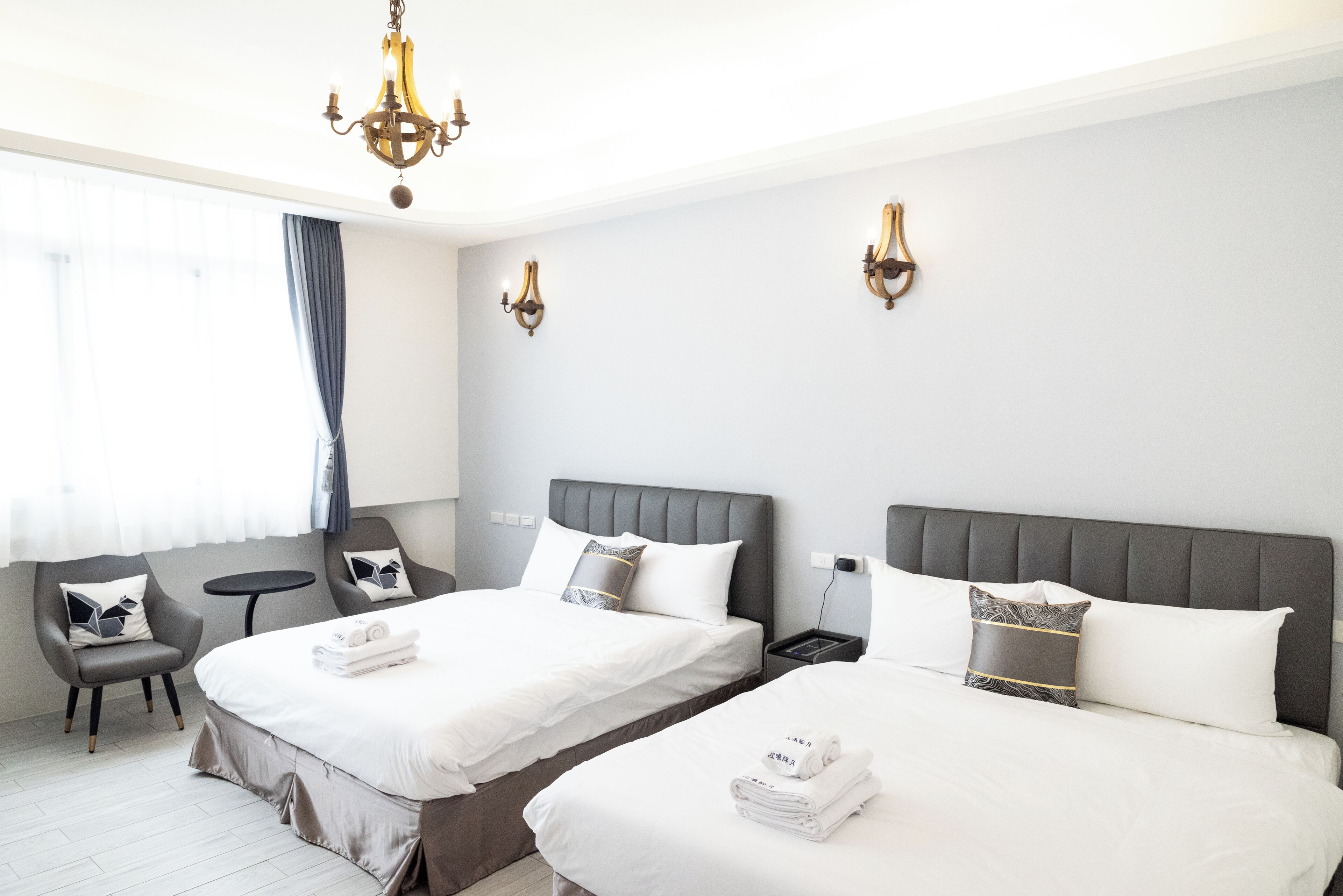 Une chambre d’hôtel avec deux lits, un coin salon comprenant un fauteuil, une petite table et un lustre.