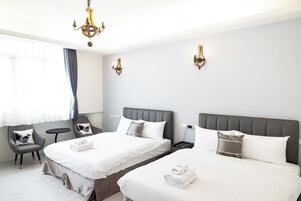 Camera d'albergo con due letti, una zona salotto con una poltrona, un tavolino e un lampadario.
