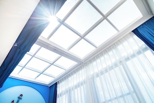 Una habitación con tragaluz, pared azul y ventana con cortinas ligeras.