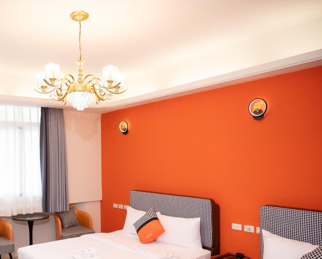 A hotel room with two beds, a chandelier, a small table, and a chair.
