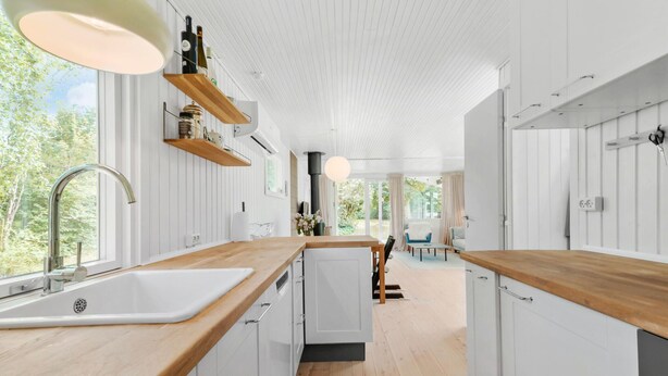 Una cucina moderna con piani in legno, mobili bianchi e un'ampia finestra con vista sul verde.