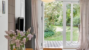 Una stanza con pavimento in legno, televisione, una pianta e una porta scorrevole in vetro che dà su un giardino.
