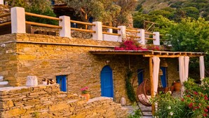 A stone building with a balcony, blue doors, and a hanging chair. - Villa Kotseli: Traditional Stone House with Pool & Sunset Sea Views (Andros)