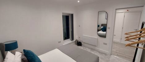 A modern bedroom with a bed, bedside table, lamp, and a mirror.