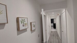 A hallway with white walls, wooden flooring, and framed botanical prints.