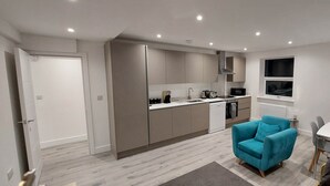 A modern kitchen with built-in appliances, a dining area with a white table and chairs, and a teal armchair.