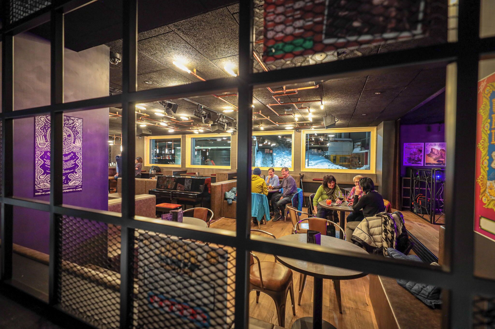 Ein Restaurant mit mehreren Tischen und Stühlen, einem Klavier und einem großen Fenster mit Blick auf die Straße.