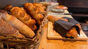 A variety of breads and pastries on a wooden table, with a small plant and a glass container in the background. - Revier Mountain Lodge Saas-Fee (Saas-Fee)