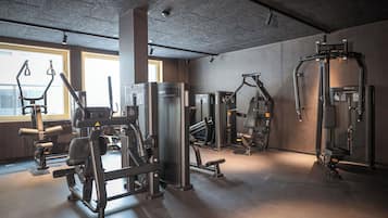 Une salle de sport équipée de divers appareils d’exercice, dotée de grandes fenêtres et d’un plafond en béton.